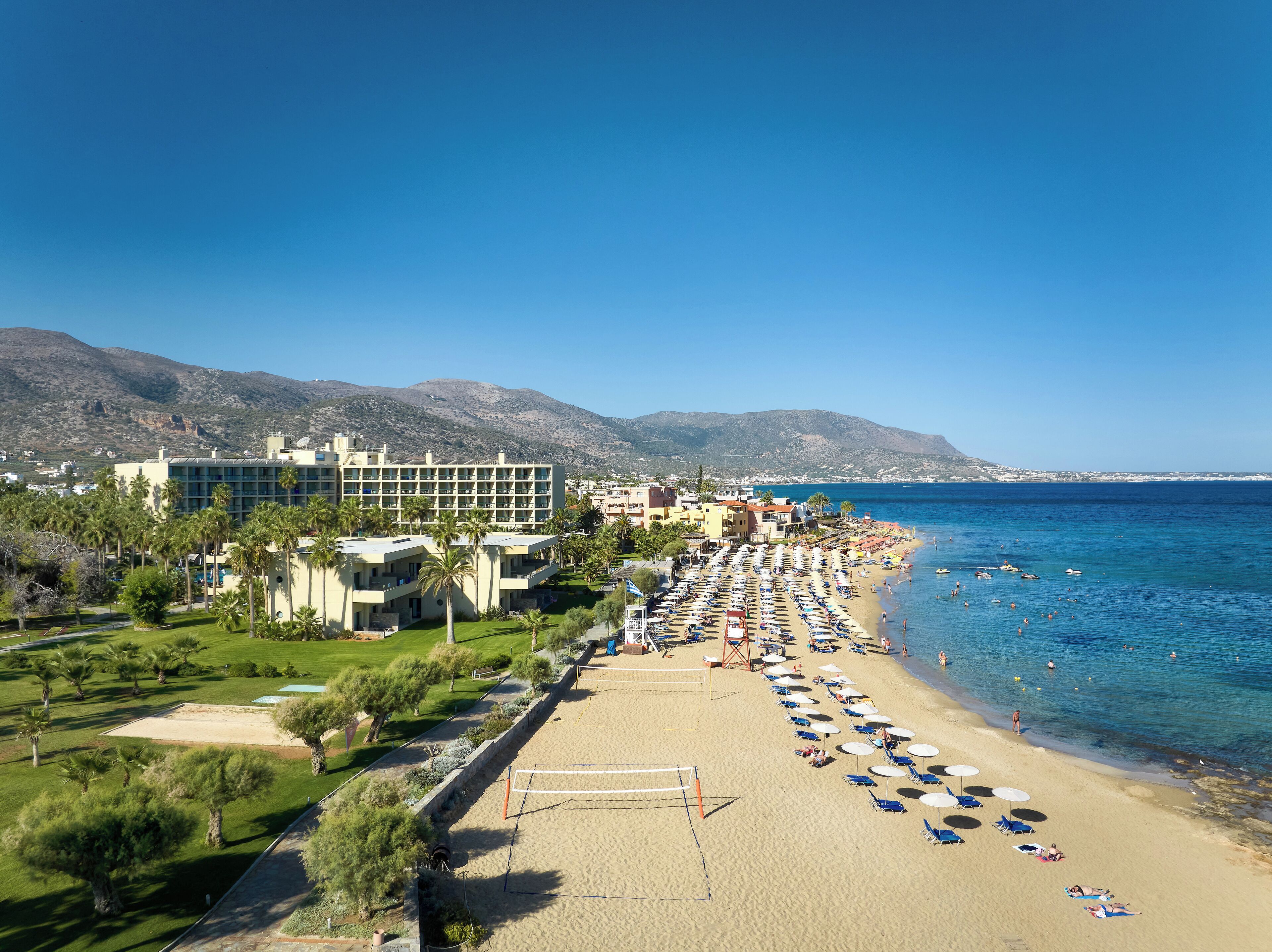 Un complejo turístico en la playa con un edificio grande, una playa de arena y un mar azul cristalino.