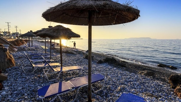 Una playa con sombrillas de paja y tumbonas.