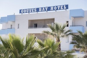 The exterior of the Gouvés Bay Hotel with a prominent sign, multiple balconies, and palm trees in the foreground. - Gouves Bay (Hersonissos)