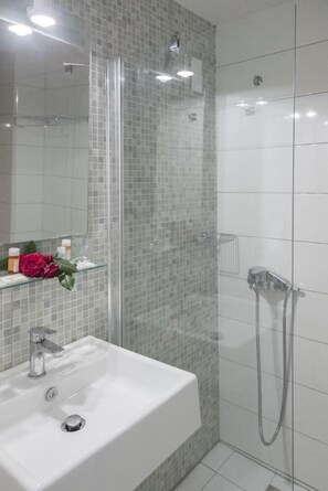 A bathroom with a glass shower enclosure, a white sink, and a mirror. - Gouves Bay (Hersonissos)
