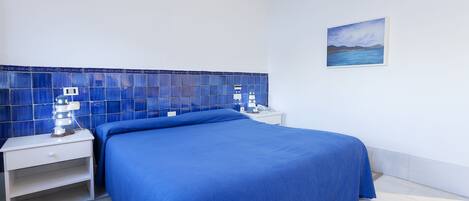 Un dormitorio con una cama, una mesita de noche, una lámpara de pared y un cuadro.