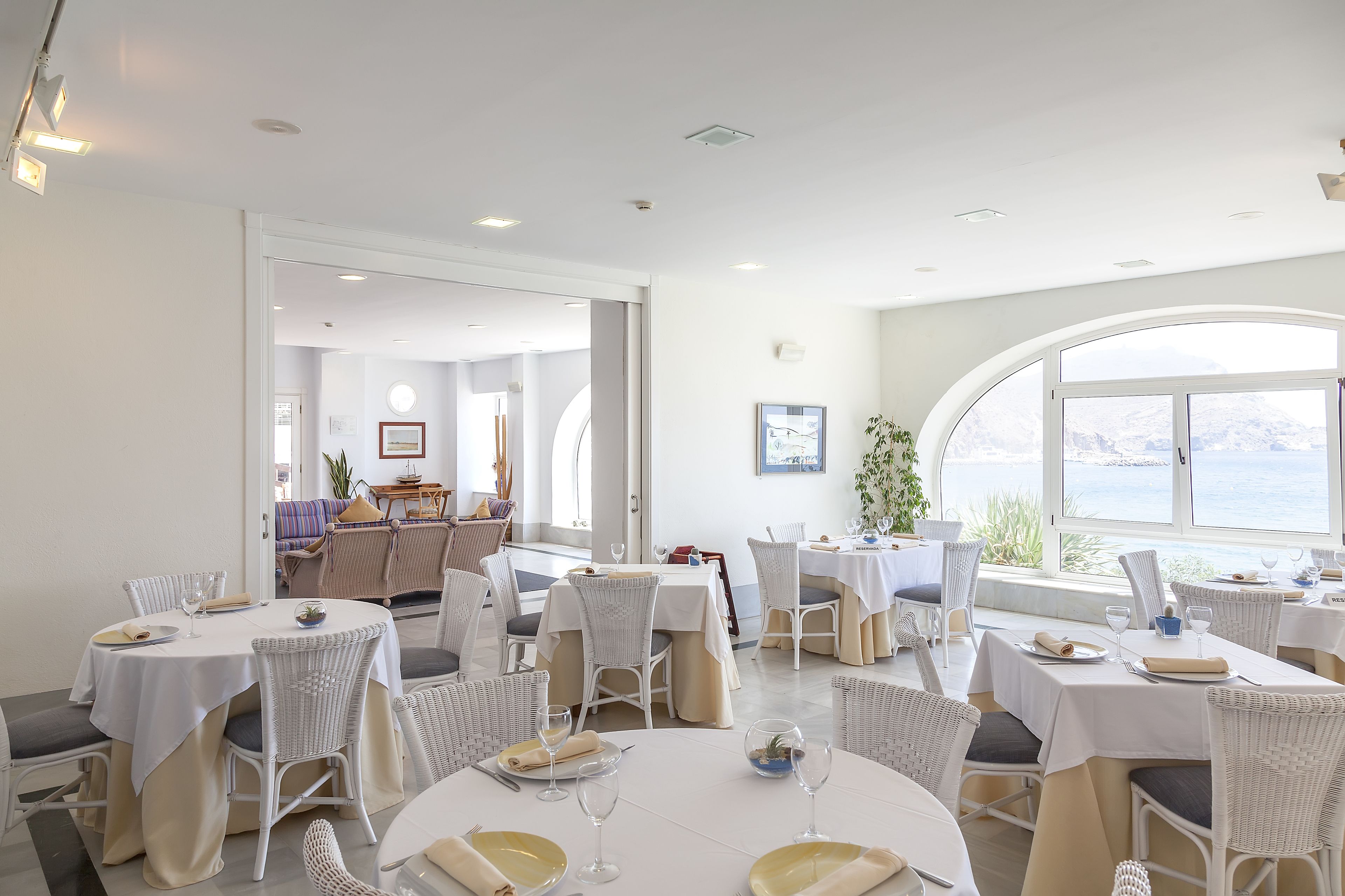 Un espace repas avec des tables rondes, des chaises blanches et une vue sur la mer.