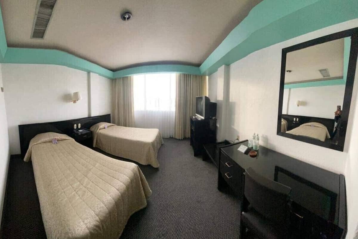 A hotel room with two beds, a desk, a TV, and a large mirror.