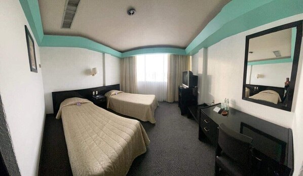 A hotel room with two beds, a desk, a TV, and a large mirror.