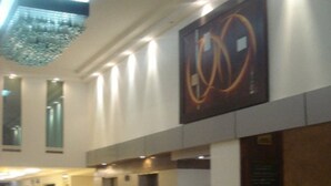 A modern lobby with a large abstract artwork, a reception desk, and a staircase leading to upper floors. - Hotel Real Rex (León)