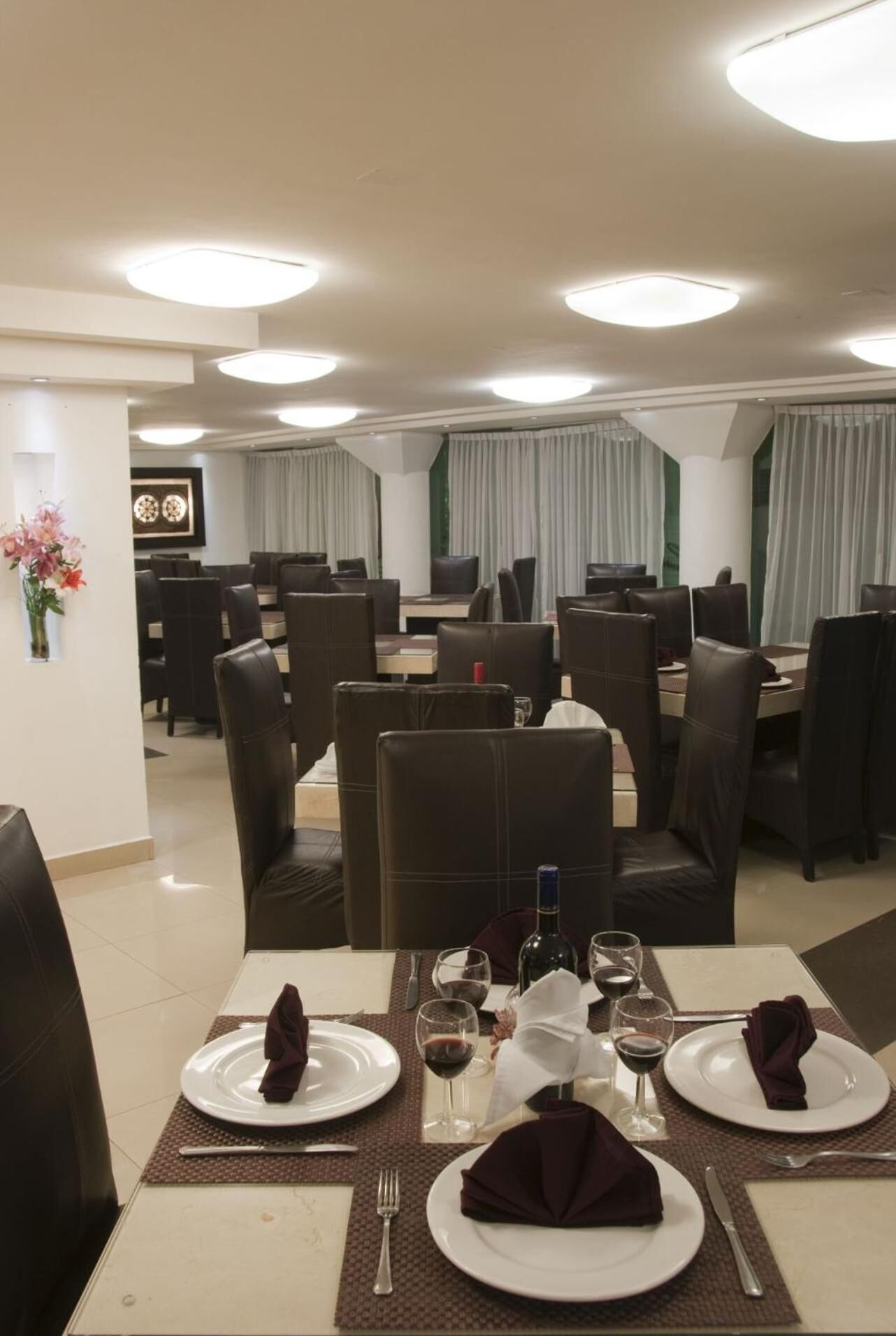 Un comedor con mesas dispuestas para dos, cada una con platos, cubiertos y copas de vino.