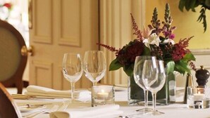 A dining table set with fine china, silverware, and clear glassware, accompanied by a vase of flowers and candles. - Ballathie Sportsmans Lodge (Perth)