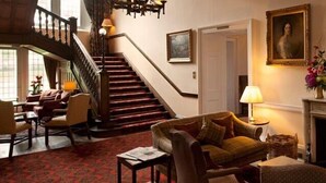 A grand staircase leading to an upper floor, a cozy sitting area with a fireplace, and a dining area with a table and chairs. - Ballathie Sportsmans Lodge (Perth)
