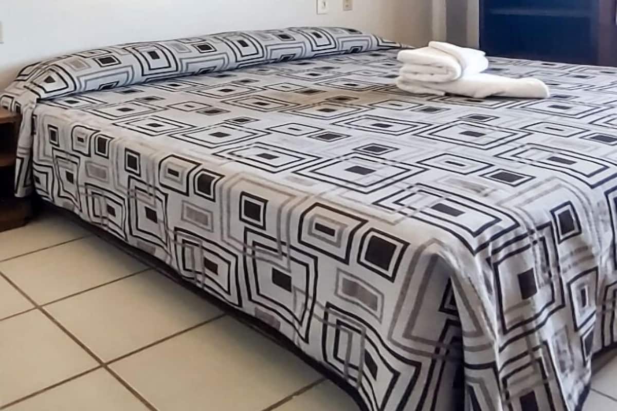 Una cama bien hecha con un edredón estampado con motivos geométricos y una toalla doblada en la cabecera.