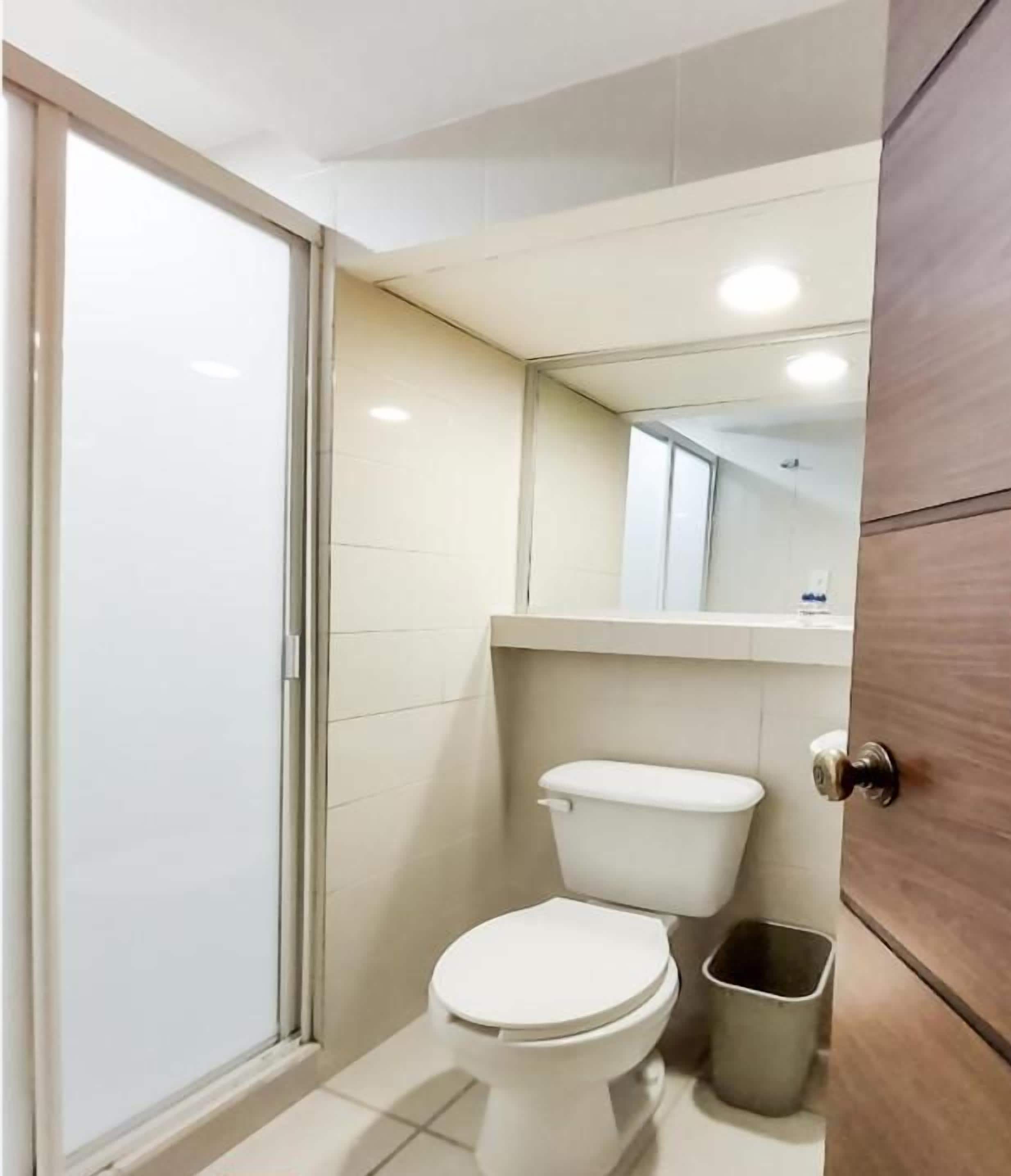 Une petite salle de bain moderne comprenant des toilettes, une poubelle et un espace douche.