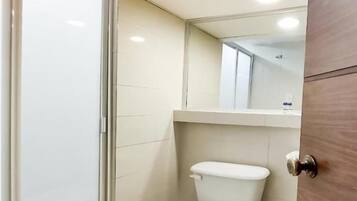 Une petite salle de bain moderne comprenant des toilettes, une poubelle et un espace douche.