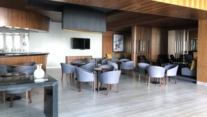 A modern lounge area with seating arrangements, a bar, and a television. - Hotel Real de Minas Bajio (León)