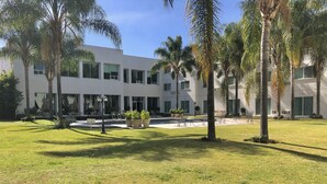 A modern building with a courtyard, palm trees, and outdoor seating areas. - Hotel Real de Minas Bajio (León)