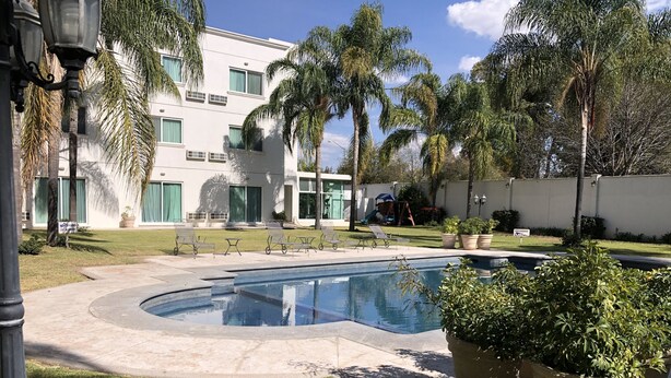 A pool area with a clear blue pool, surrounded by palm trees and a well-maintained lawn. - Hotel Real de Minas Bajio (León)