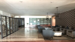A spacious lobby with a marble floor, seating area with sofas and armchairs, a reception desk, and a wall with a patterned design. - Hotel Real de Minas Bajio (León)