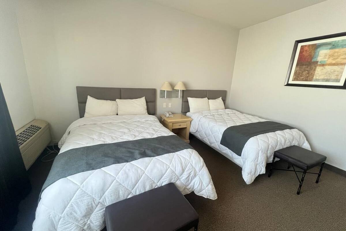 A hotel room with two beds, a bedside table with a lamp, a heater, and a framed picture on the wall.