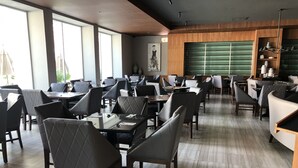 A modern restaurant with a mix of booth and table seating, large windows, and a green sliding door. - Hotel Real de Minas Bajio (León)