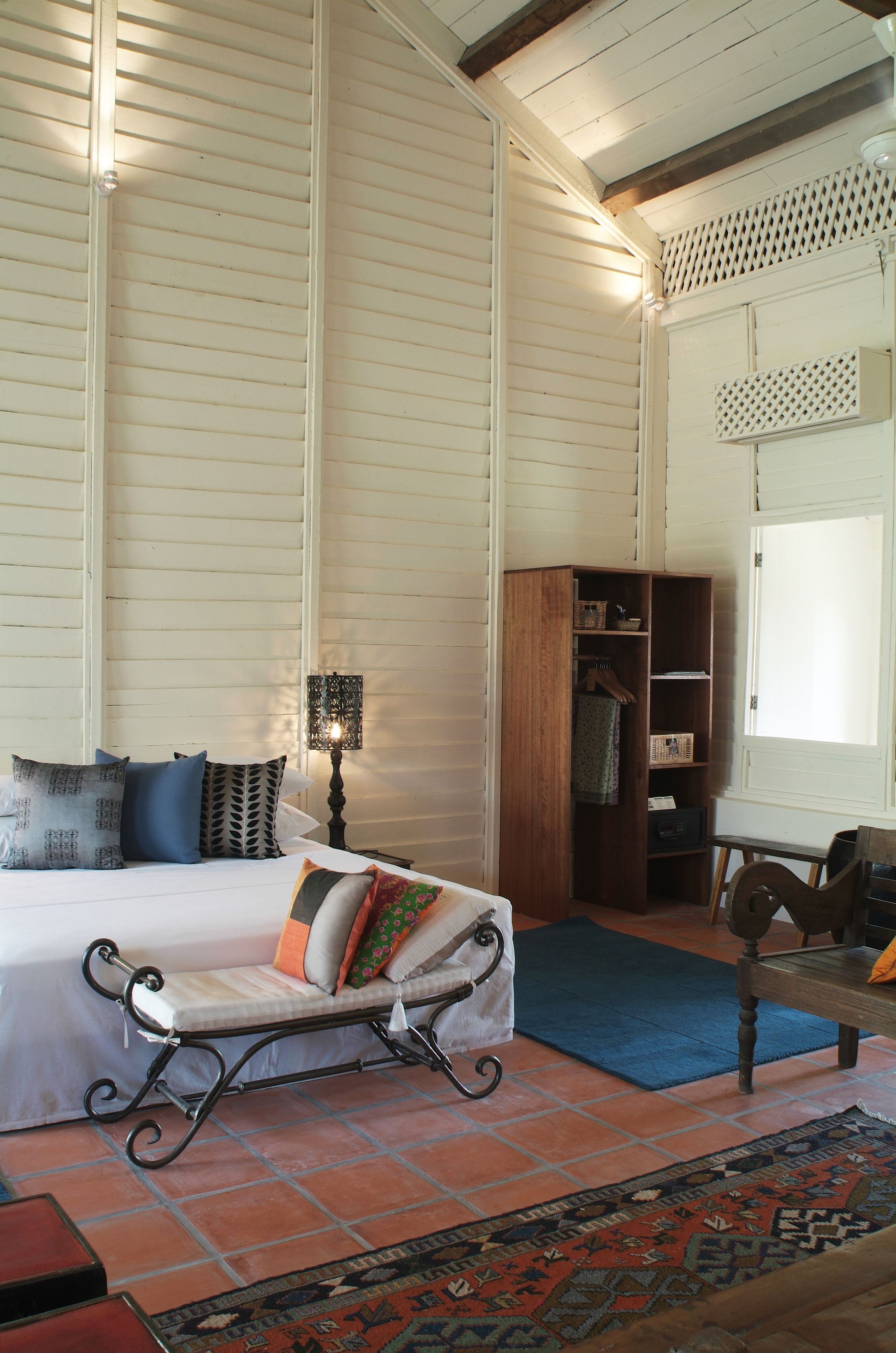 A bedroom with a bed, a wooden wardrobe, a bench, a lamp, and a patterned rug.