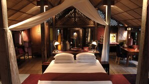 Una cama con sábanas blancas, un escritorio de madera y una silla en una habitación con techo y paredes de madera.