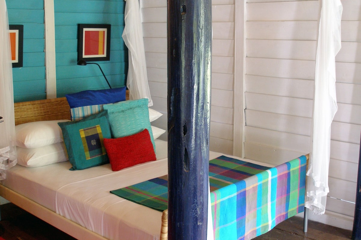 Un letto singolo con una coperta a quadri colorata, una testiera in legno e un baldacchino bianco.