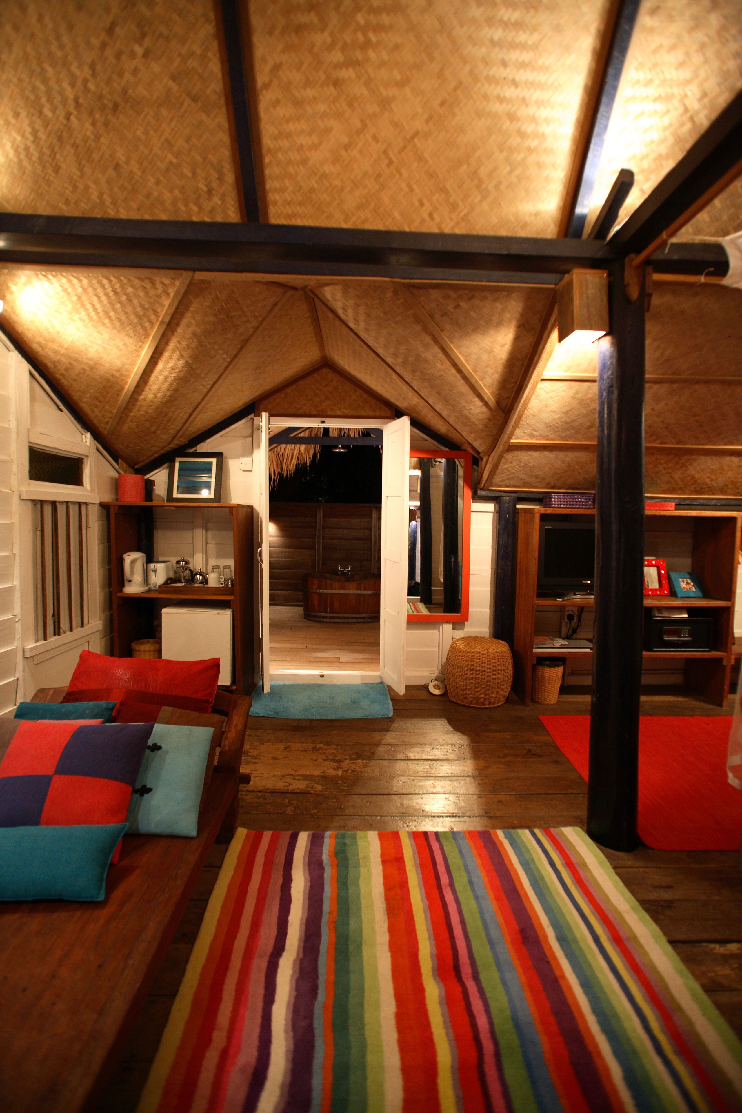 A cozy attic bedroom with a sloped ceiling, wooden beams, a bed with colorful pillows, a small table, and a bookshelf.