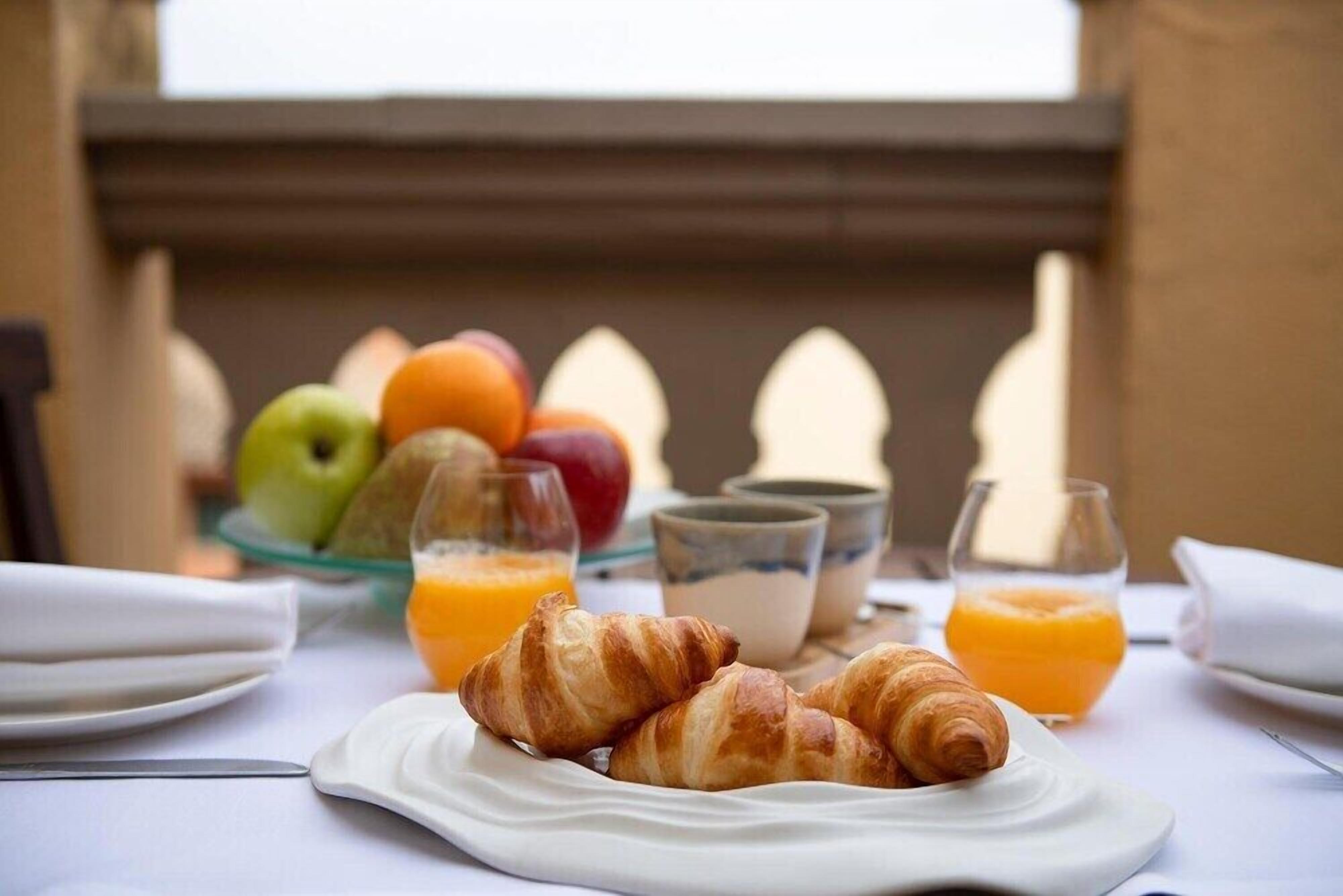 A breakfast setting with croissants, fruit, and orange juice on a table.