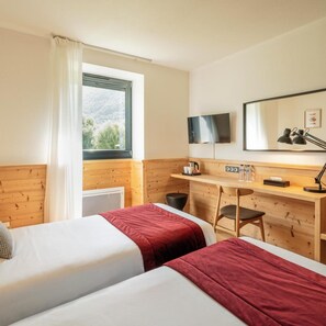 Een hotelkamer met twee bedden, een bureau, een stoel, een televisie en een raam met uitzicht op bomen.