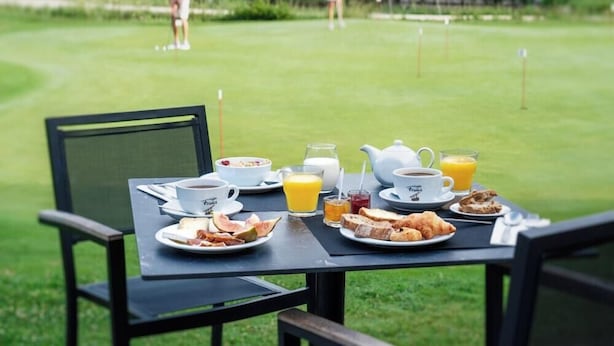 Une table de petit-déjeuner avec du café, du jus de fruits et des viennoiseries, installée sur un terrain de golf.