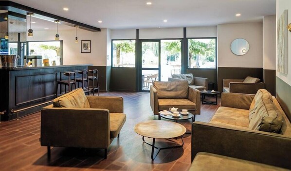 Ein moderner Lounge-Bereich mit Ledersofas, einem Couchtisch und einer Bar mit Hockern. Große Fenster sorgen für natürliches Licht und Ausblicke ins Freie.