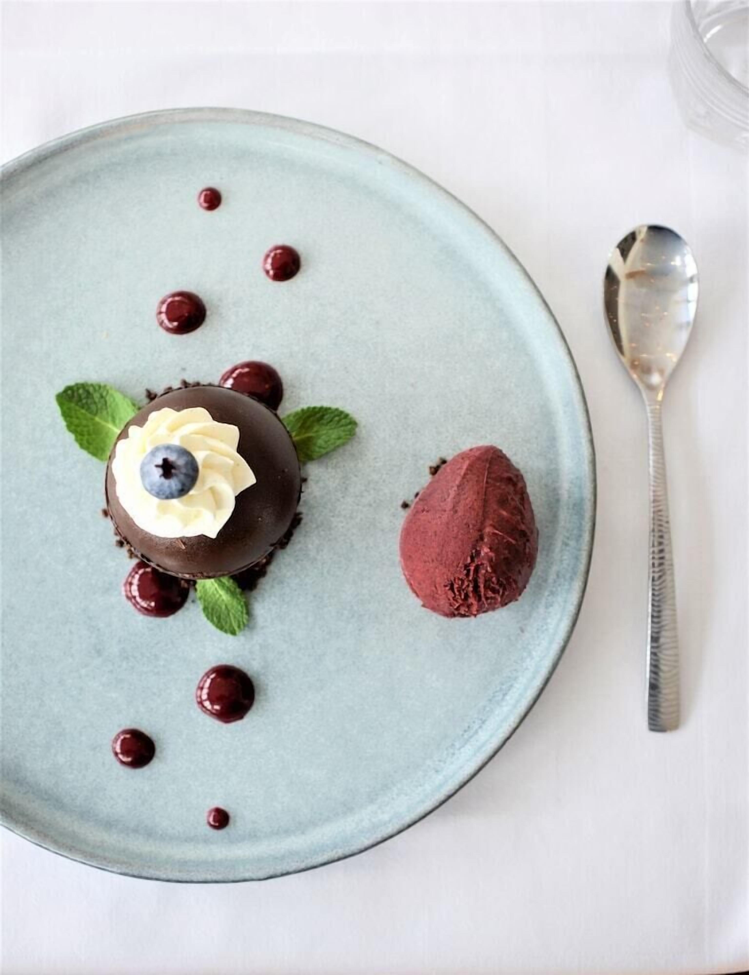 A dessert plate with a chocolate sphere, a scoop of red ice cream, and cherries.