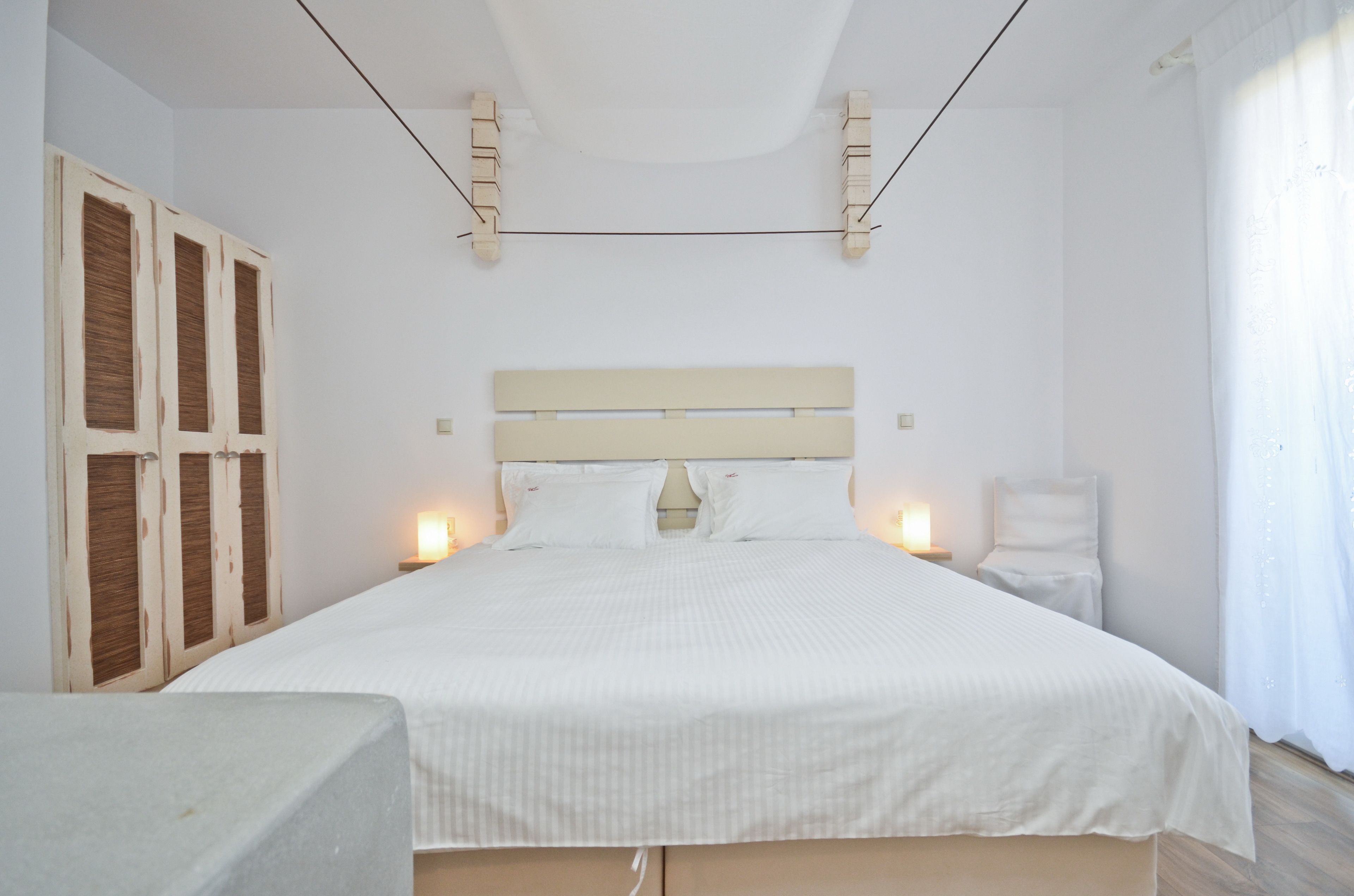 A bedroom with a large bed, wooden wardrobe, bedside tables, and a ceiling light fixture.