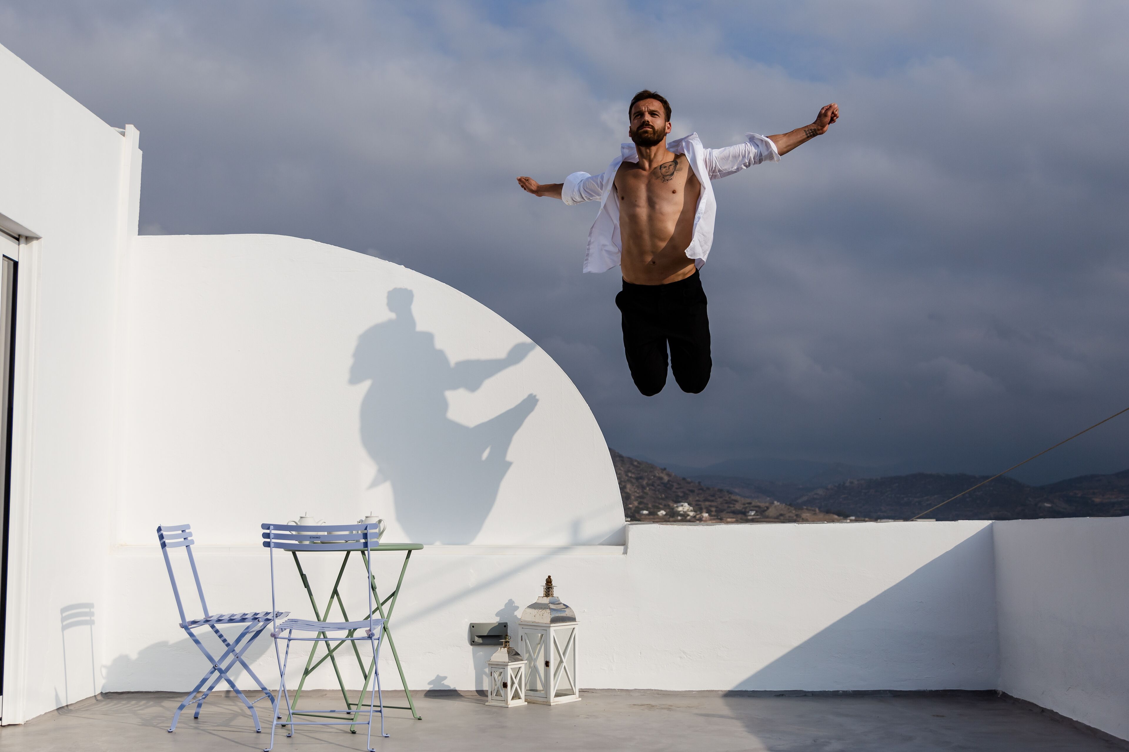 Une personne sautant sur un toit, avec un mur blanc et une table entourée de chaises.