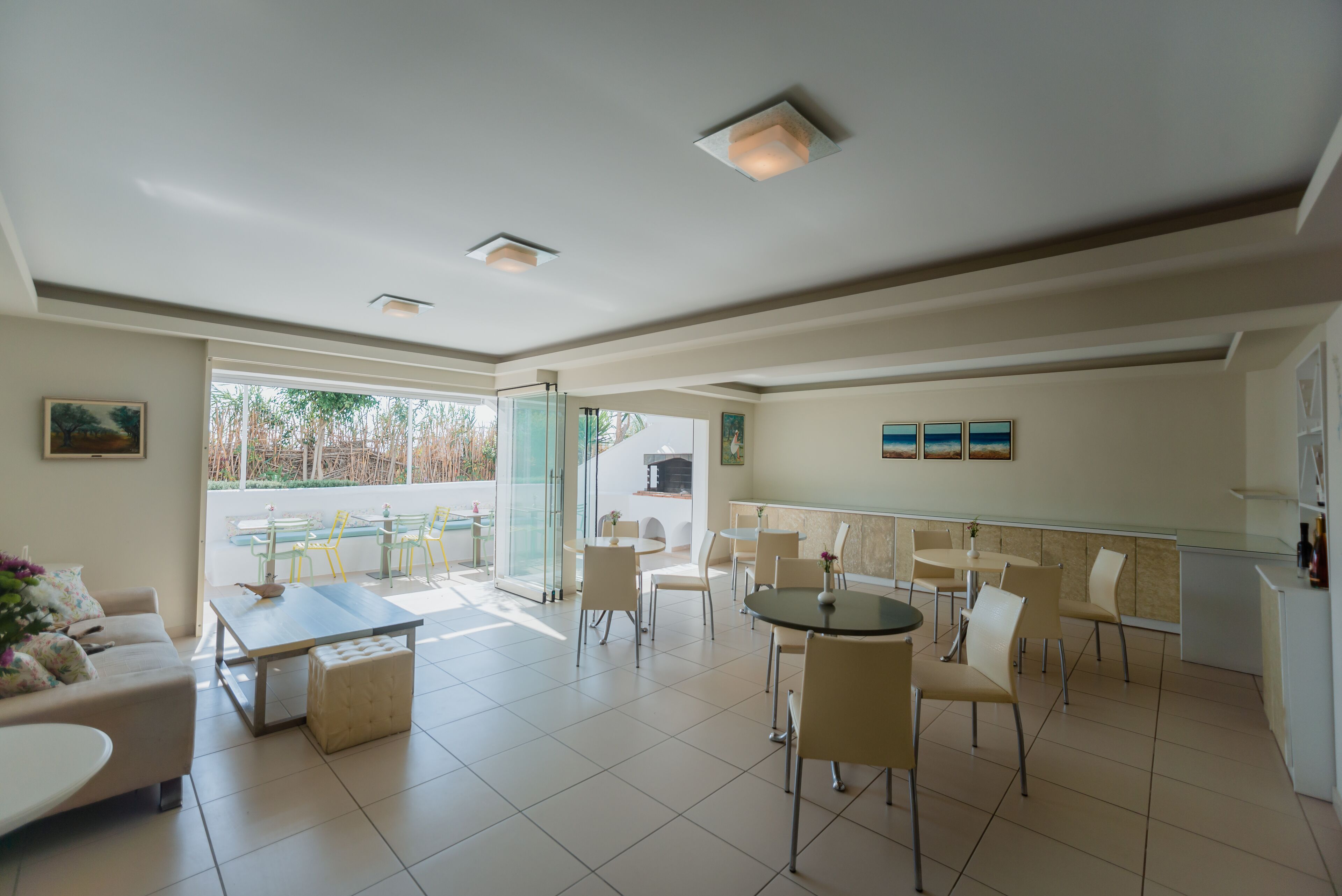 A spacious dining area with multiple tables and chairs, a sofa, and a kitchen area visible through an open door.