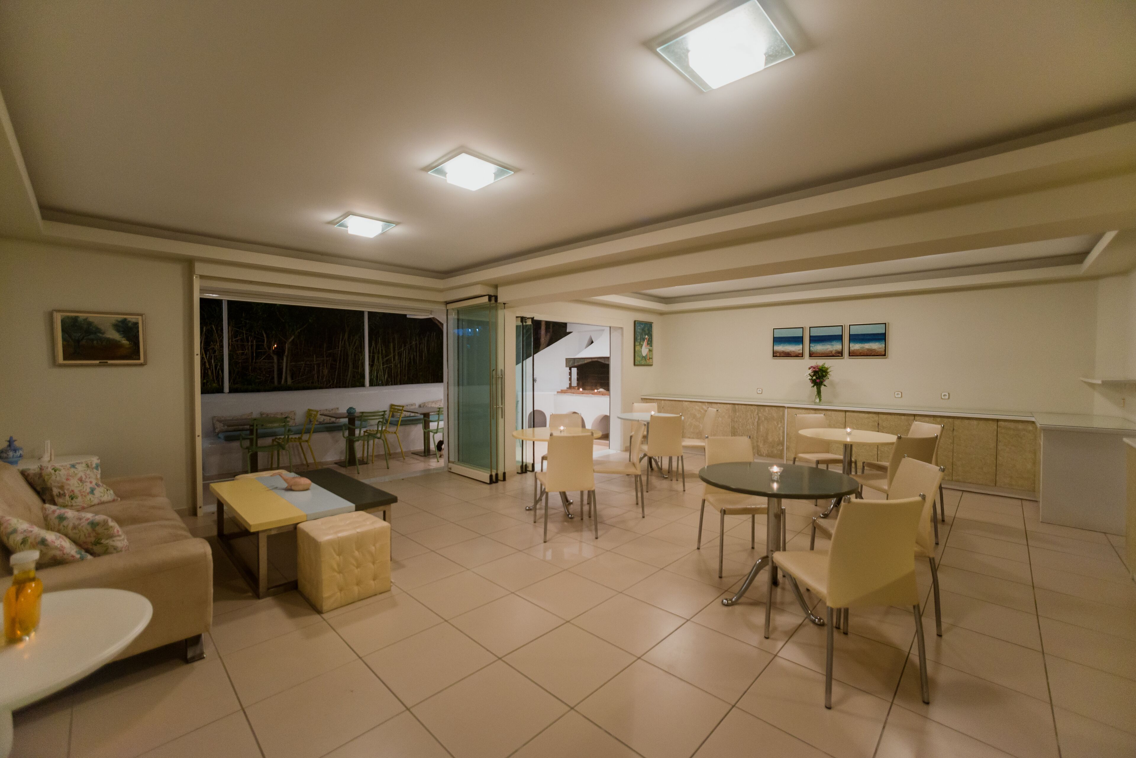A spacious living area with a sofa, coffee table, and dining table set for four. There is a kitchen area in the background with a staircase leading to an upper level.