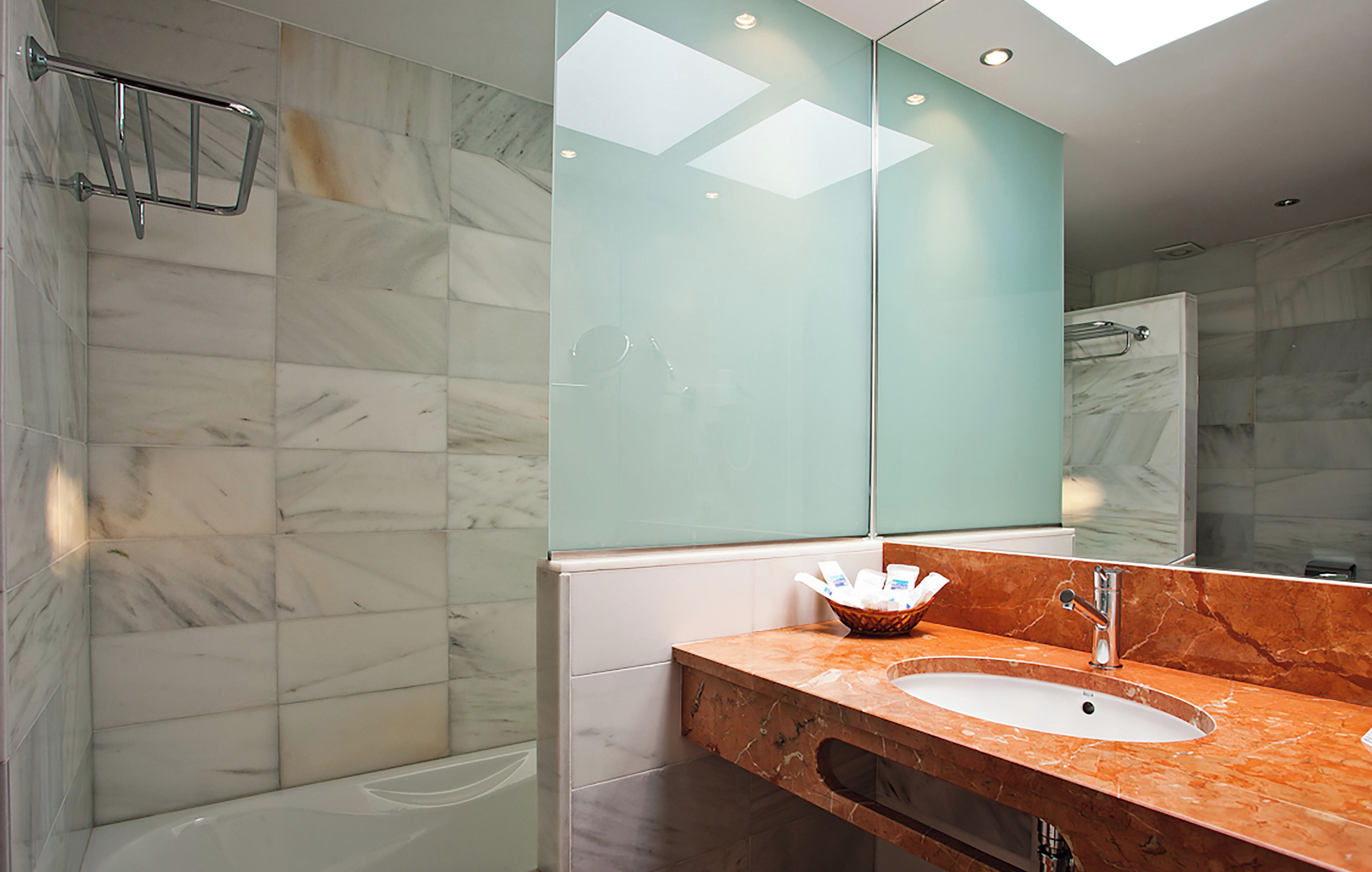 Ein modernes Badezimmer mit einer Duschkabine aus Glas, einer marmorverkleideten Wand und einem Waschbecken mit Marmorplatte.