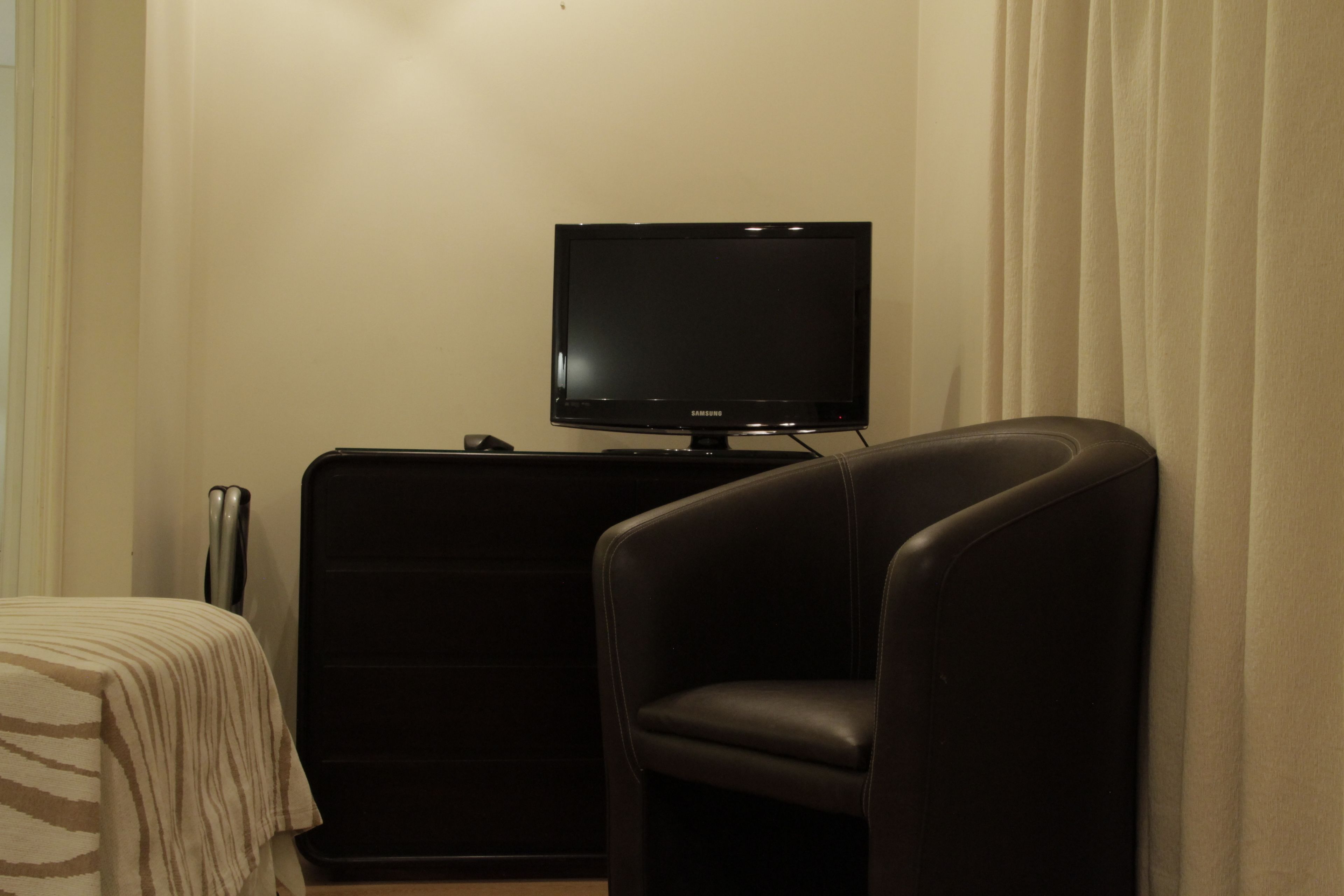 A room with a television on a stand, a black chair, and a bed with a striped blanket.