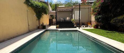 Una piscina con agua cristalina, rodeada por un muro bajo y un pequeño patio con muebles de exterior.
