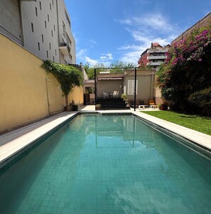 Una piscina con agua cristalina, rodeada por un muro bajo y un pequeño patio con muebles de exterior.