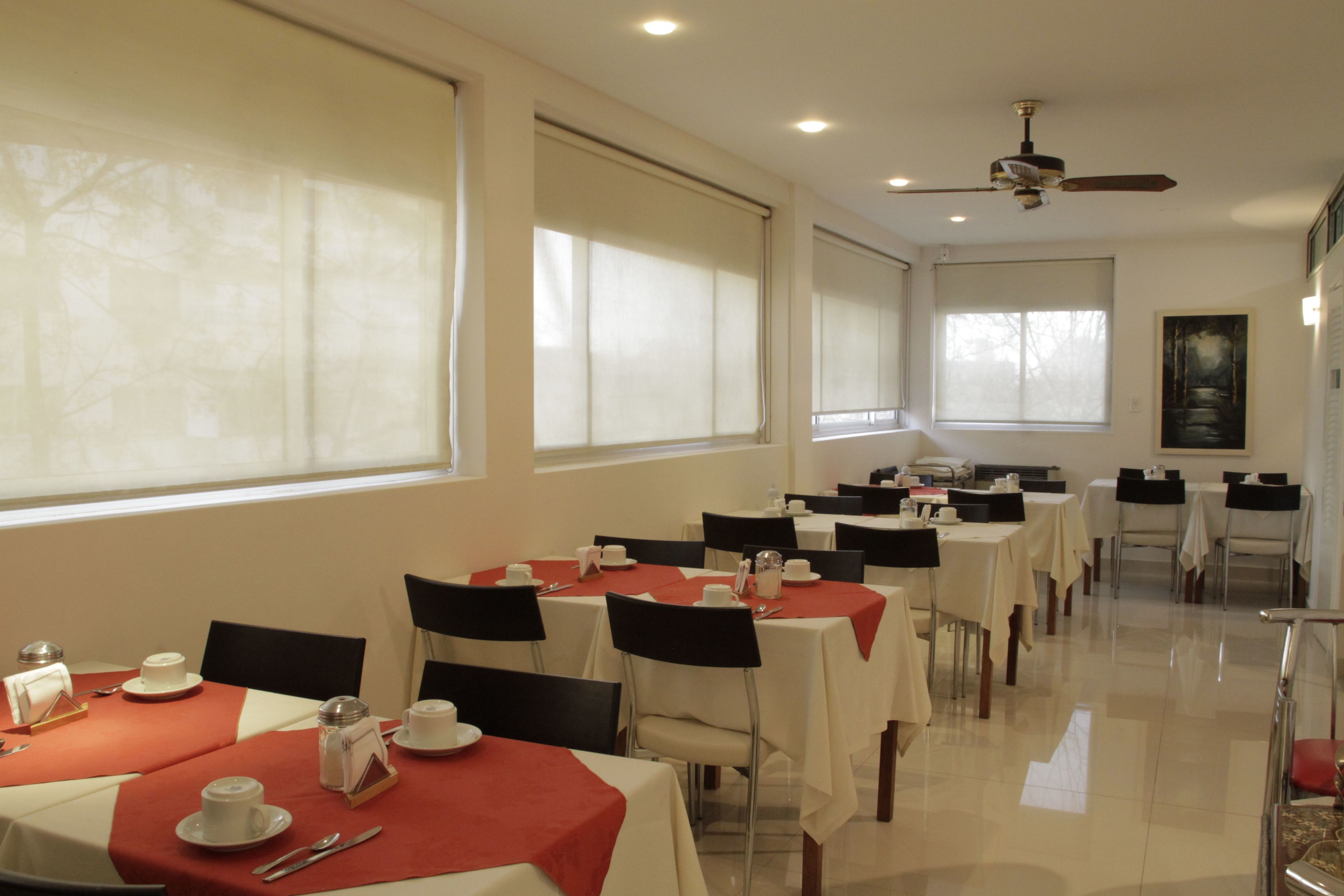 A hotel dining area with multiple tables set for breakfast, featuring white tablecloths and red napkins.