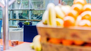 Un coin repas avec une table dressée pour deux personnes, un saladier de fruits et une vue sur l’extérieur grâce à de grandes fenêtres.