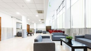 Un hall d’entrée spacieux avec des canapés gris, une table basse noire et une plante en pot.