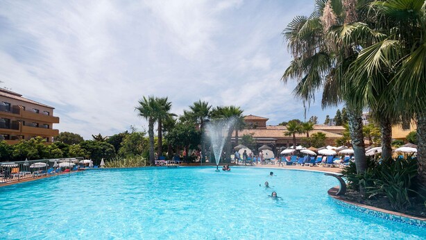 Une piscine avec une fontaine, entourée de palmiers et de chaises longues.