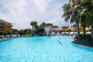 Una piscina con fuente, rodeada de palmeras y sillas de descanso.