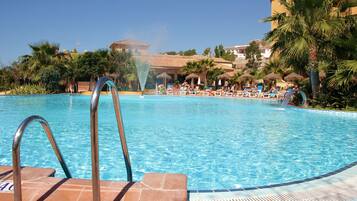 Una piscina con fuente, sillas de descanso y palmeras.