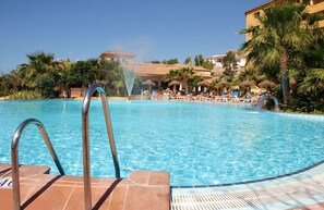 A swimming pool with a water fountain, lounge chairs, and palm trees. - Hotel Best Alcazar (Almunecar)