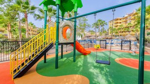 Une aire de jeux avec un toboggan, des balançoires et une structure d’escalade.