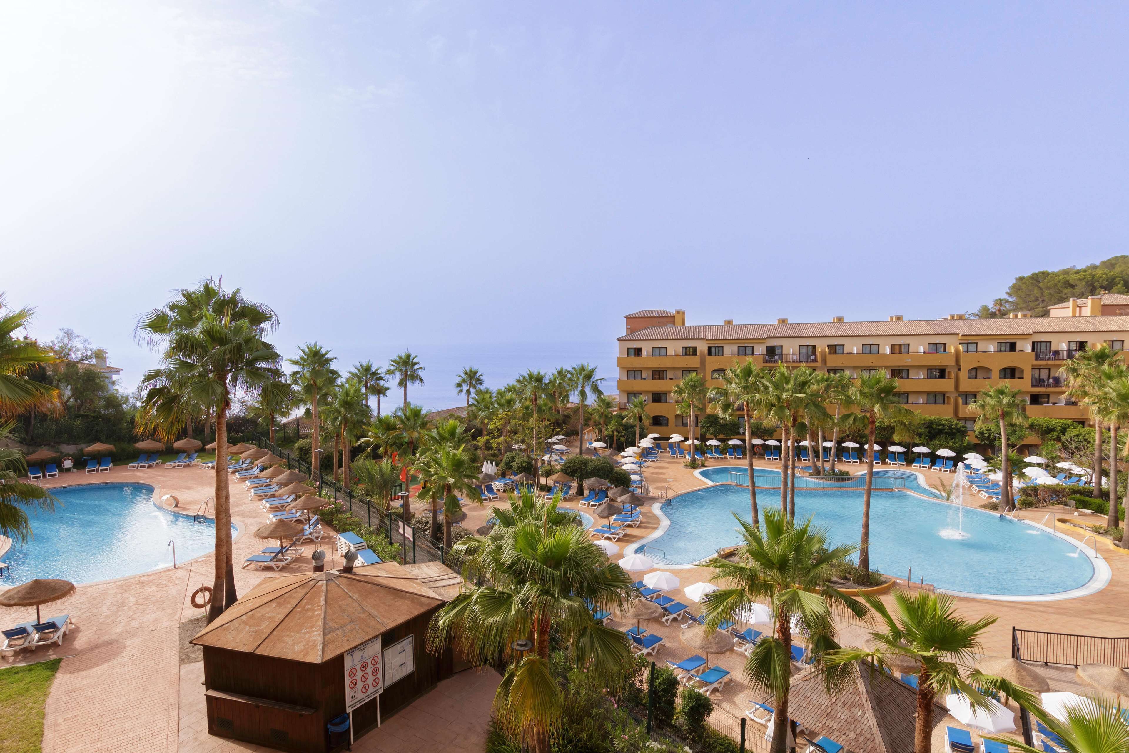 A resort with multiple swimming pools, palm trees, and sun loungers.
