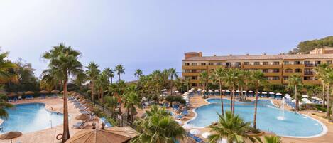 A resort with multiple swimming pools, palm trees, and sun loungers.