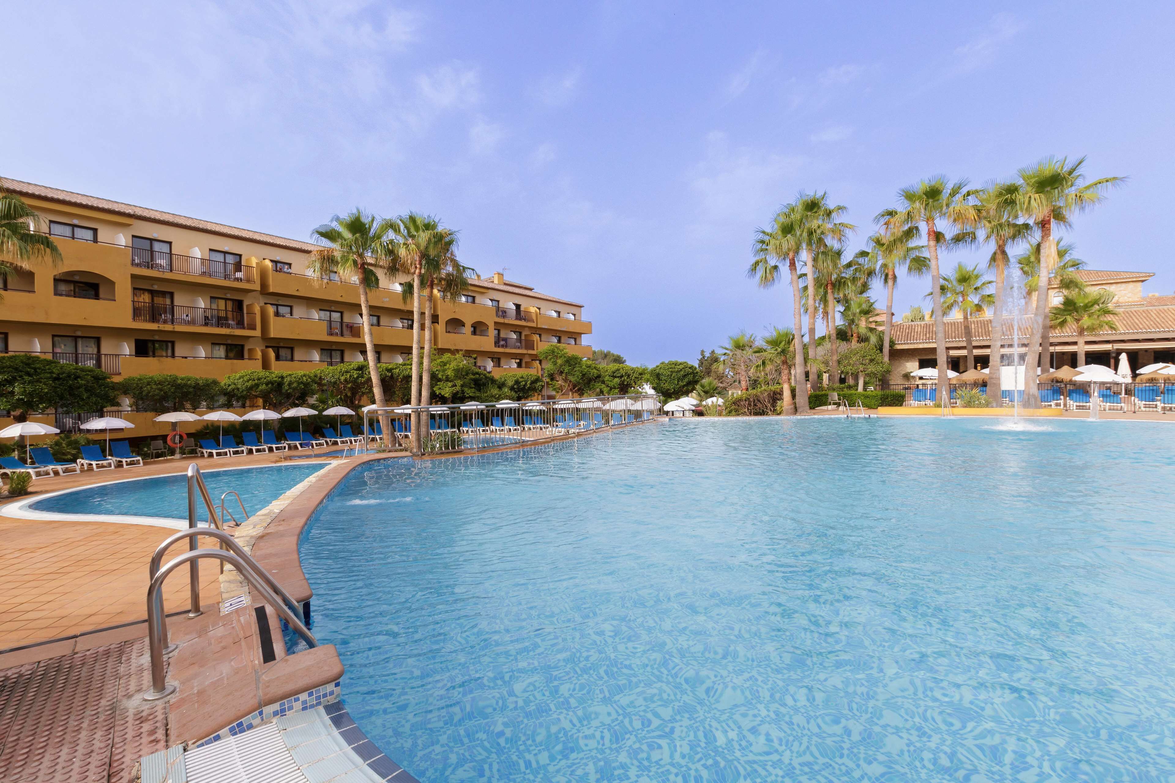 Un hotel con piscina, palmeras y tumbonas.