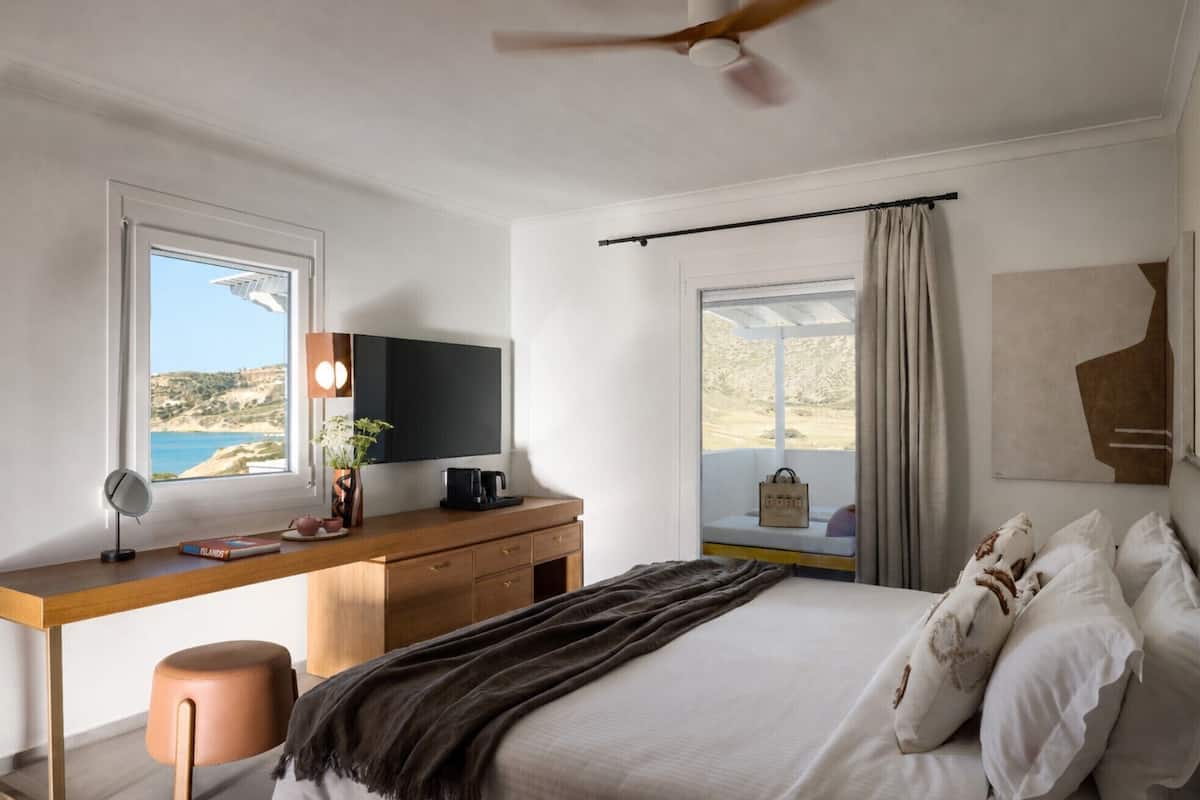 Un dormitorio con cama, escritorio, televisor y vista al mar.